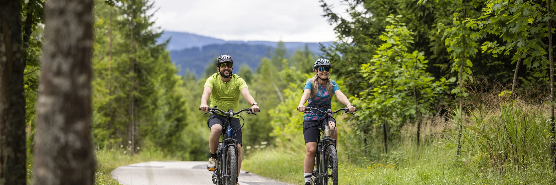 Two cyclists riding on a rural road through a green forest