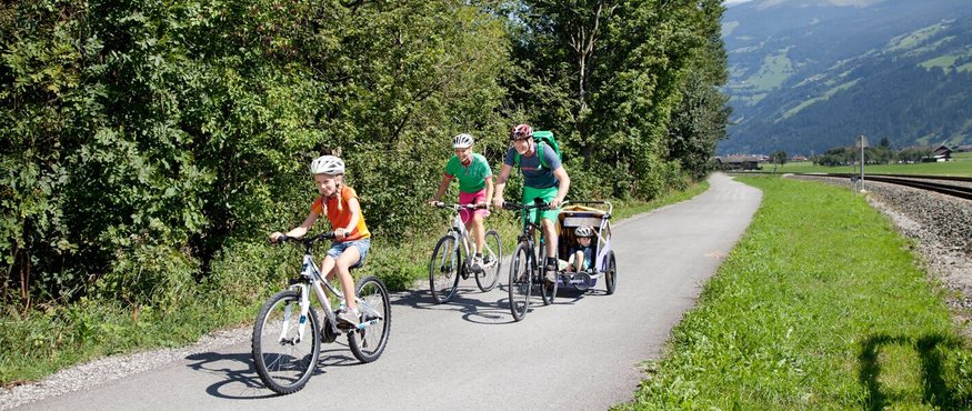 Family cycling on a path beside trees and mountains