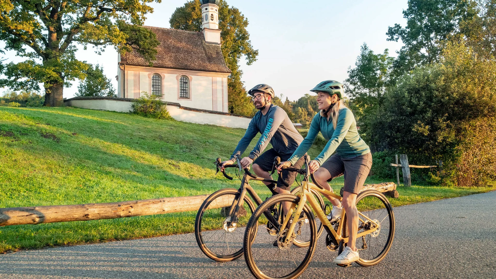 Twee fietsers rijden langs een kleine kerk op een groene landweg