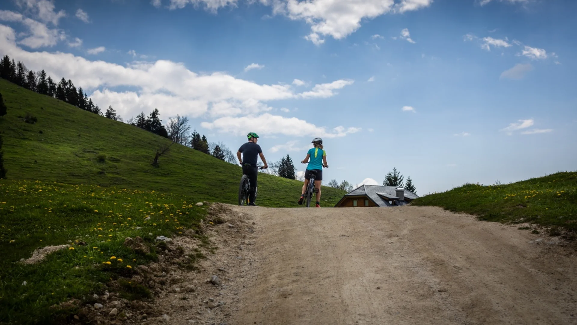 Twee fietsers op een bergpad met groen gras en bewolkte hemel
