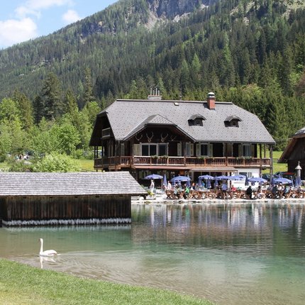 House by lake with terrace and guests near forested mountain hills