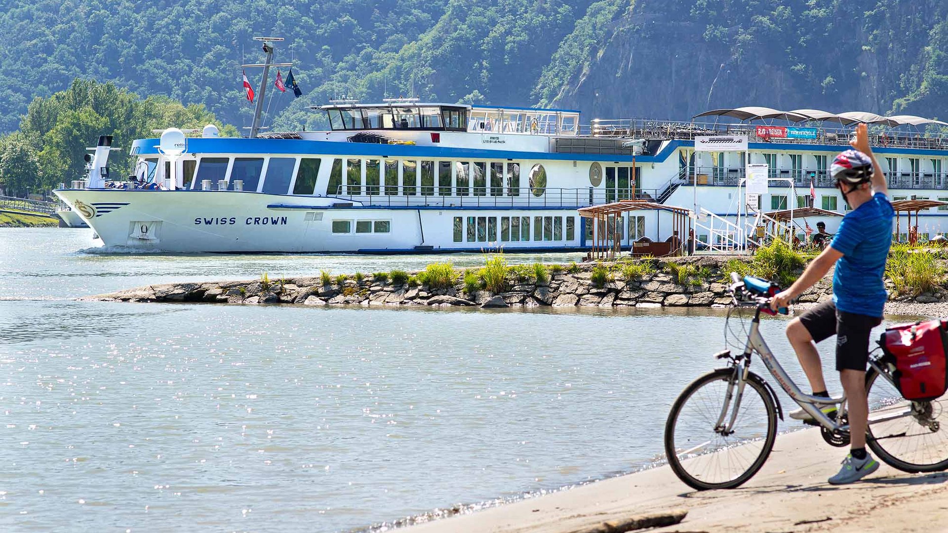 Cyclist waving at passing Swiss Crown passenger ship on river