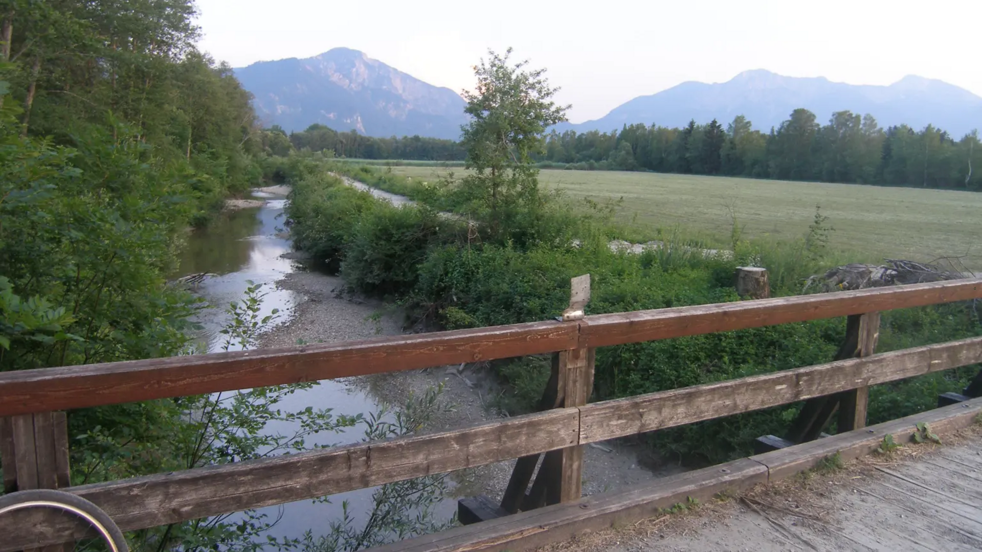 Wooden bridge over a stream with mountains and fields in the background