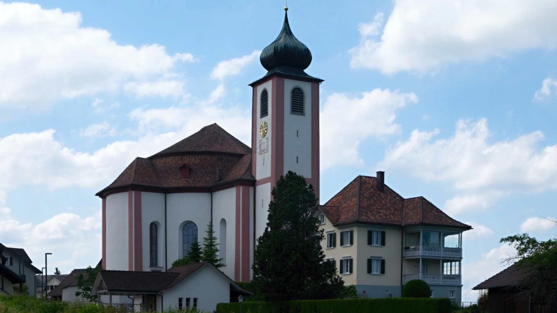 Kirche mit Zwiebelturm und angrenzendem Haus unter blauem Himmel