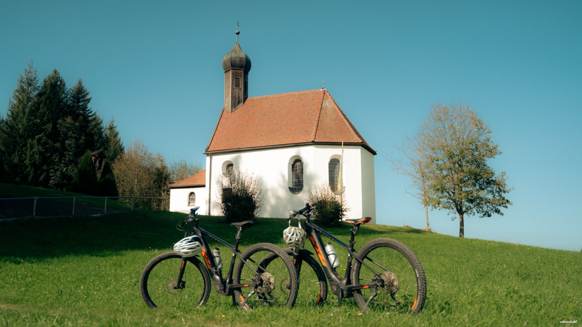 Two bicycles in front of a small church on a green hill on a sunny day