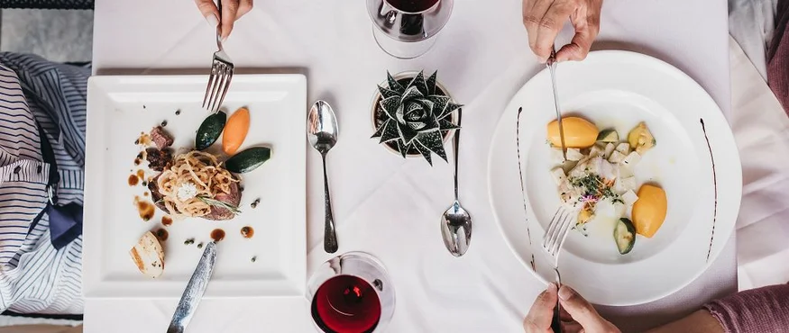 Zwei Personen essen feines Essen mit Rotwein an einem weiß gedeckten Tisch