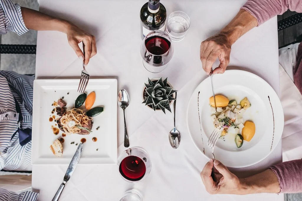 Kulinarik © Heldentheater Zwei Personen essen feines Essen mit Rotwein an einem weiß gedeckten Tisch