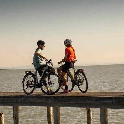 Twee fietsers op een steiger boven het water bij zonsondergang
