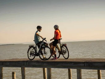 Lake Neusiedl © Velontour Two cyclists standing with bicycles on a pier by the water at sunset