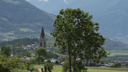 Ein Genuss-Radtag am Reschensee © IDM Südtirol - T. Grüner Zwei Radfahrer auf Landstraße vor Dorf und verschneiten Bergen