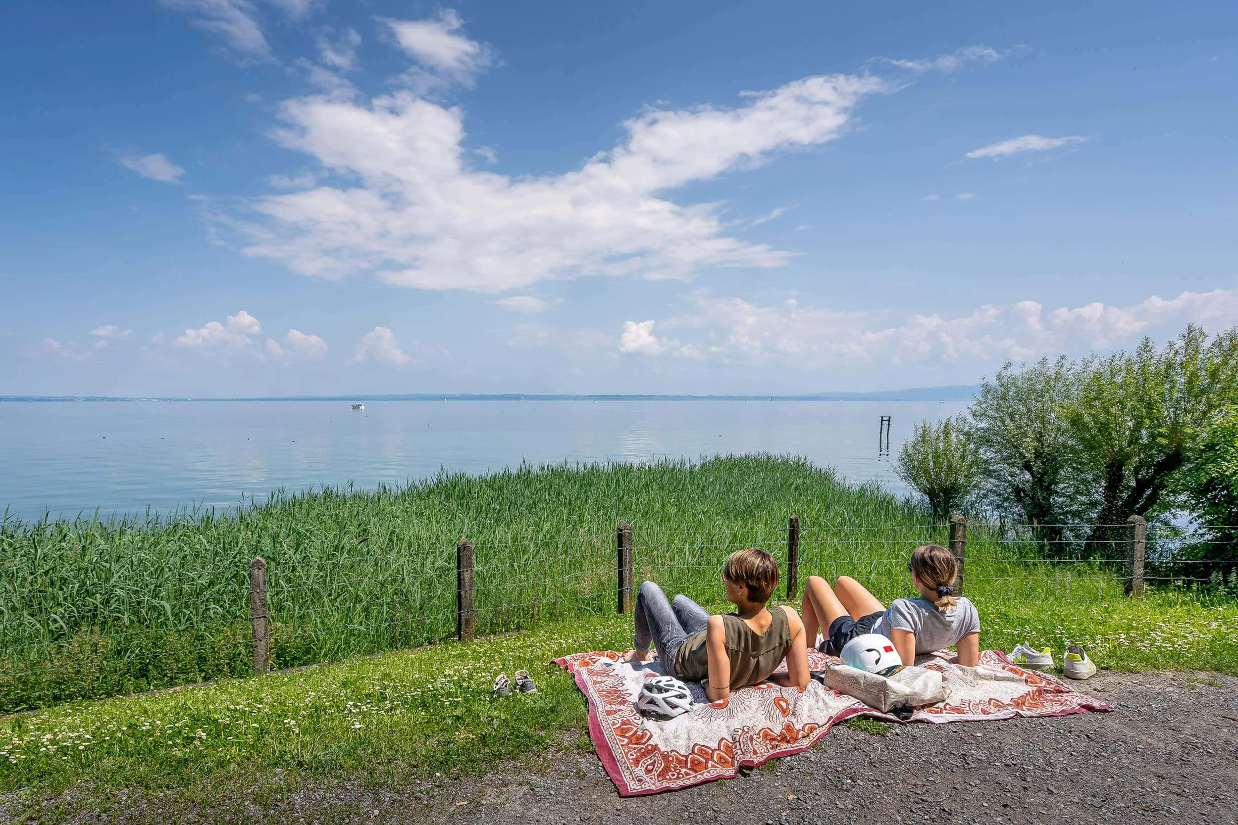 Zwei Personen liegen auf Decken und genießen den Blick auf einen See und Himmel