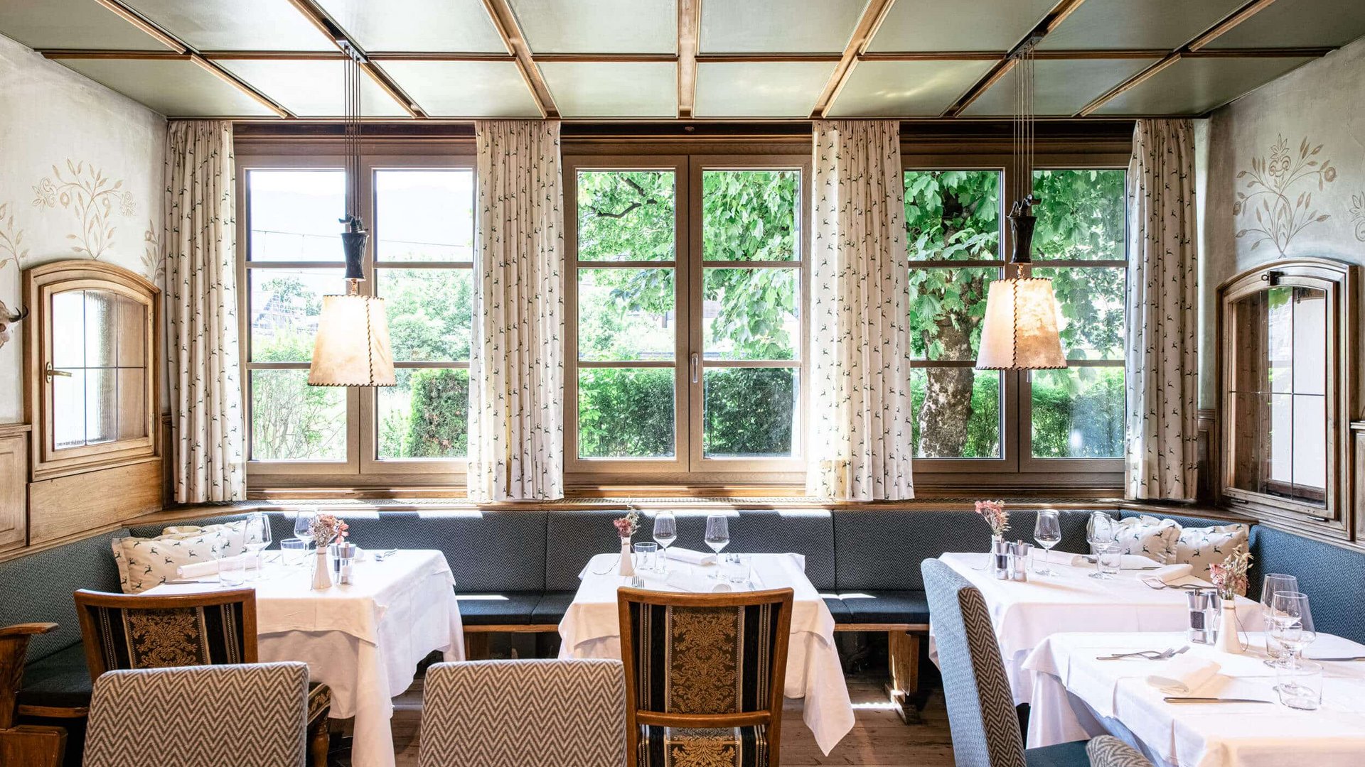 Bright restaurant with white tablecloths and large windows showing green trees