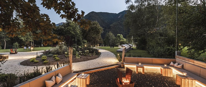Lit garden with seating area and fire pit in front of mountain backdrop at dusk