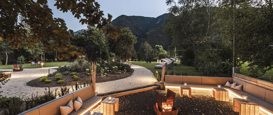 Lit garden with seating area and fire pit in front of mountain backdrop at dusk