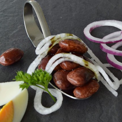 Spoon with red beans, onion rings, egg slices, and parsley on black surface