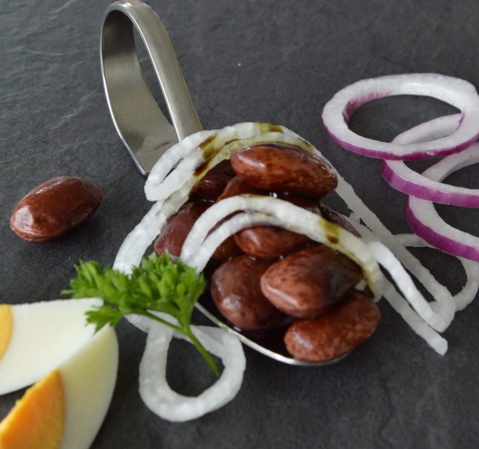 Spoon with red beans, onion rings, egg slices, and parsley on black surface