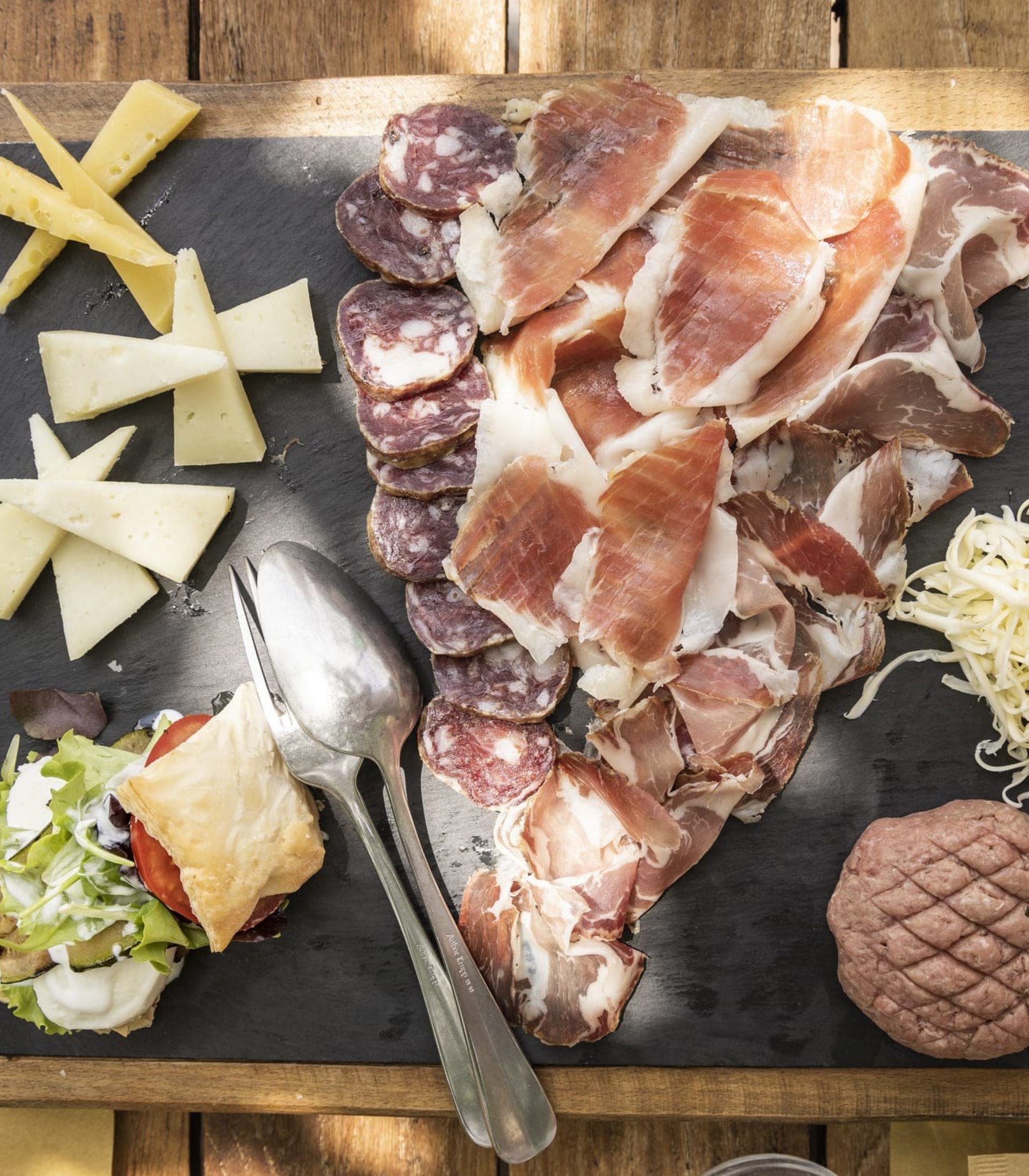 Wooden board with assorted cheeses, cold cuts, and salad
