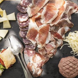 Wooden board with assorted cheeses, cold cuts, and salad