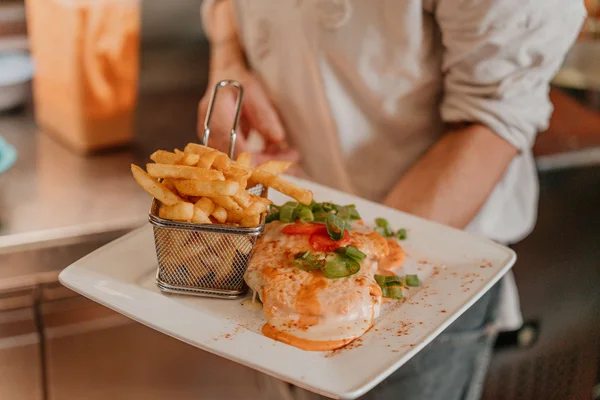 Teufelstoast © Tourismusverein Inn-Salzach Person serviert Teller mit Pommes und mit Sauce überzogenem Gericht
