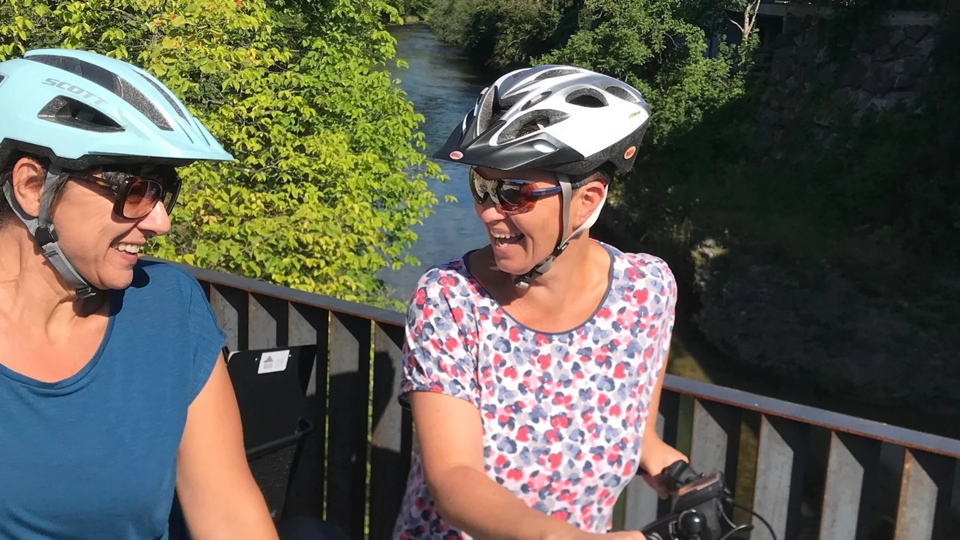 Tour-Detail Zwei Frauen mit Fahrradhelmen auf einer Brücke bei sonnigem Wetter