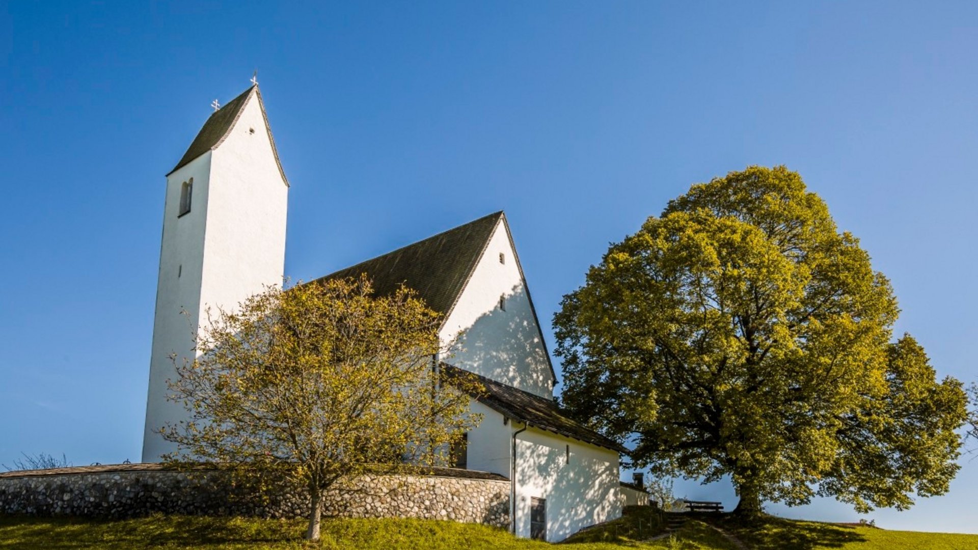 White church with tower on green hill under clear blue sky