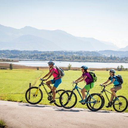 Three cyclists riding on a country road by a lake and mountains