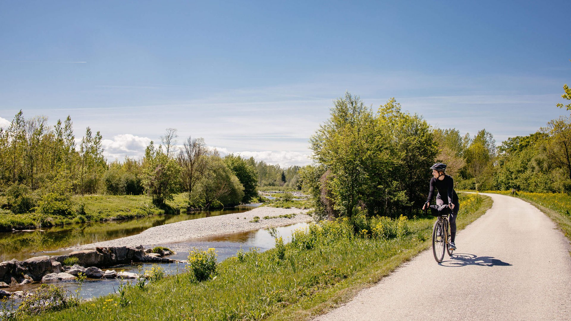 Cyclist on riverside path on a sunny day surrounded by green nature