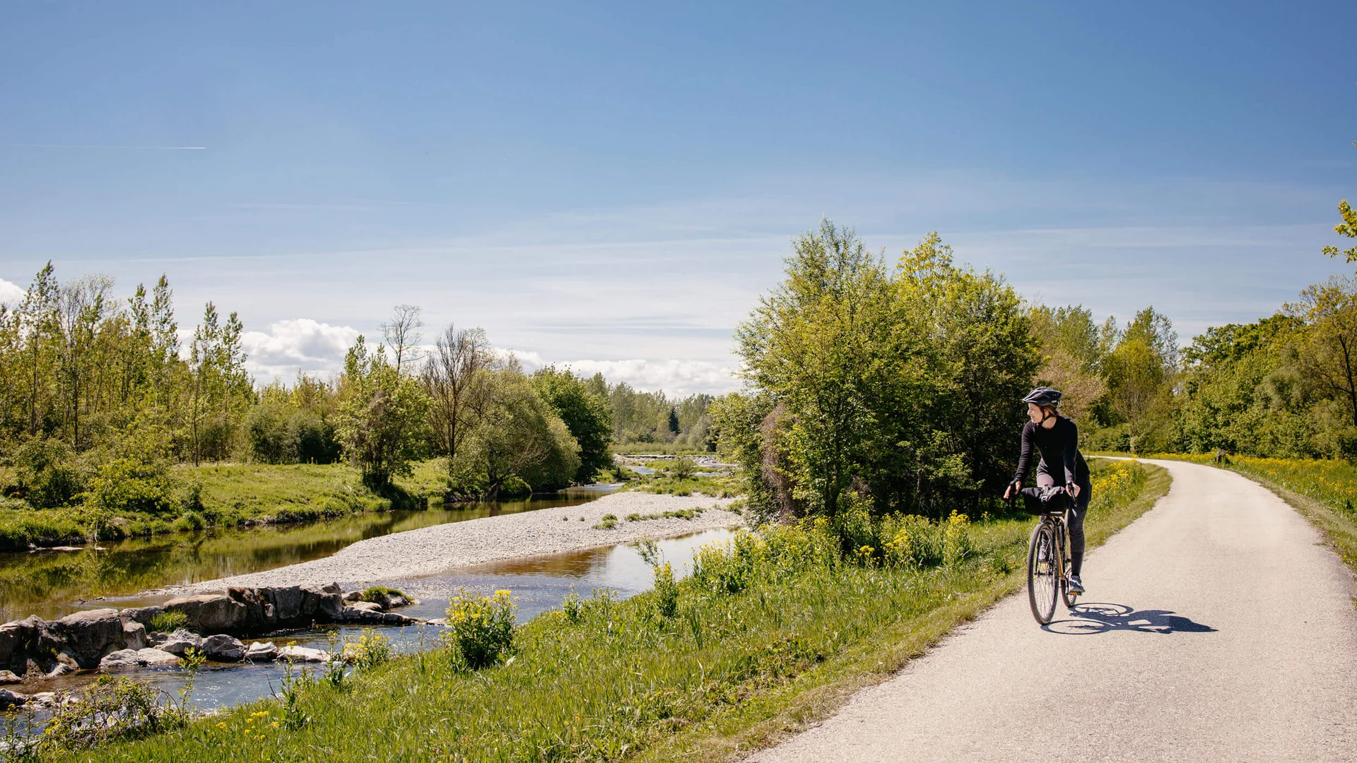 Fahrradfahrer auf Flussweg bei sonnigem Wetter umgeben von grüner Natur