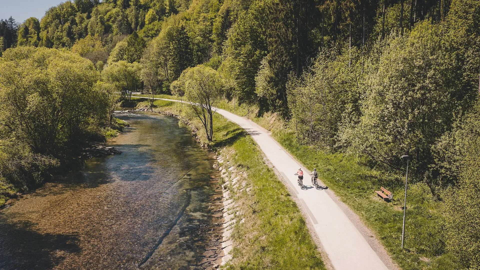 Tour-Detail Zwei Radfahrer auf einem Weg neben einem Fluss im grünen Wald