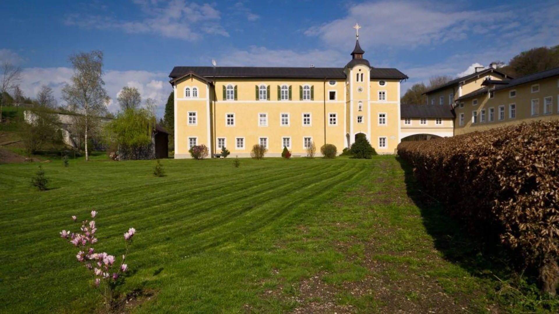 Tour-Detail © Gerald Fimberger Gelbes Klostergebäude mit Turm vor grünem Rasen und blühendem Strauch