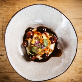 Gourmet dish with breaded item, sauce, and edible flowers on white plate