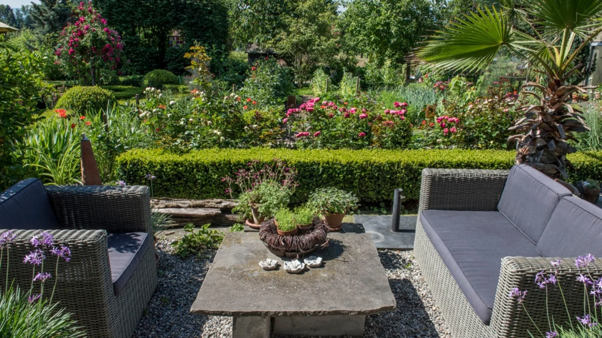 Tuin met twee grijze rotan stoelen en een stenen tafel in het midden
