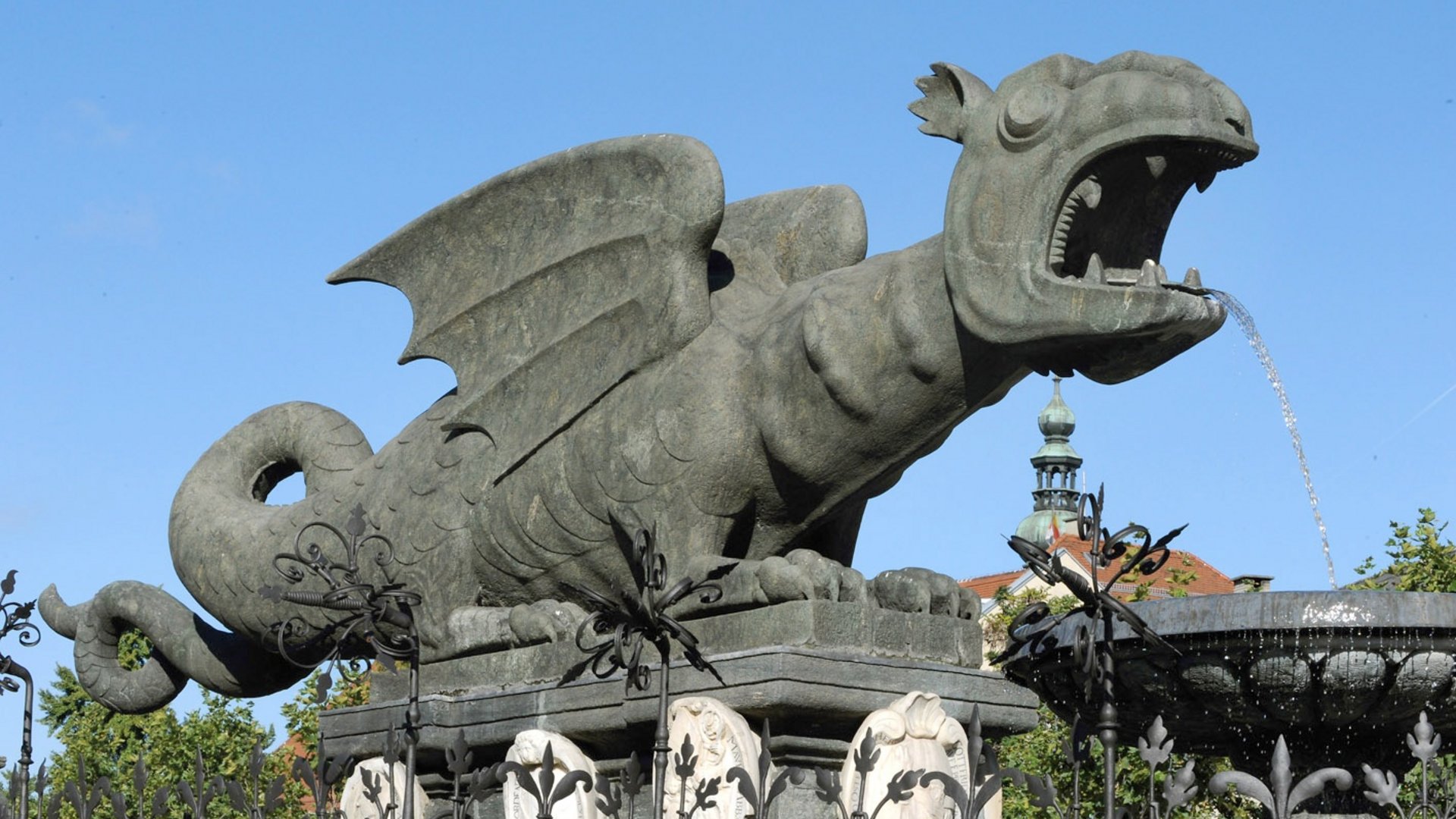 Stone dragon fountain spouting water against blue sky