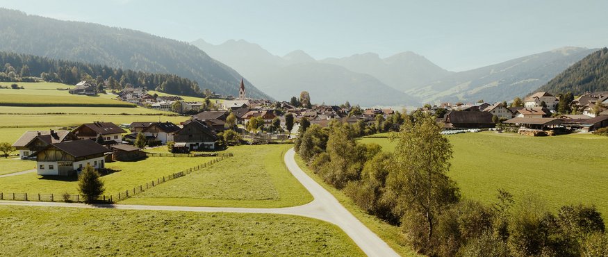 Bicyclists on rural road through green valley with village and mountains