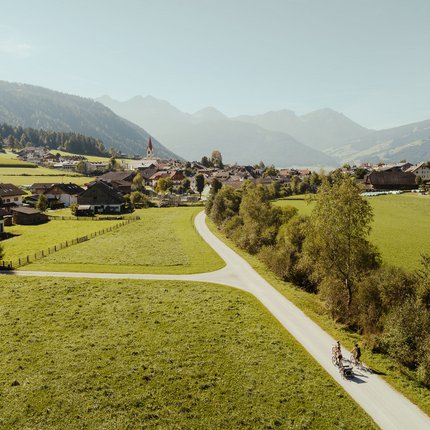 Bicyclists on rural road through green valley with village and mountains