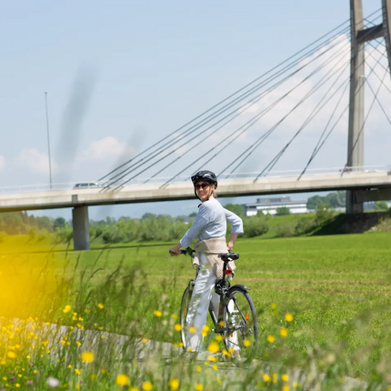 Woman with bicycle on path next to meadow with yellow flowers near a bridge