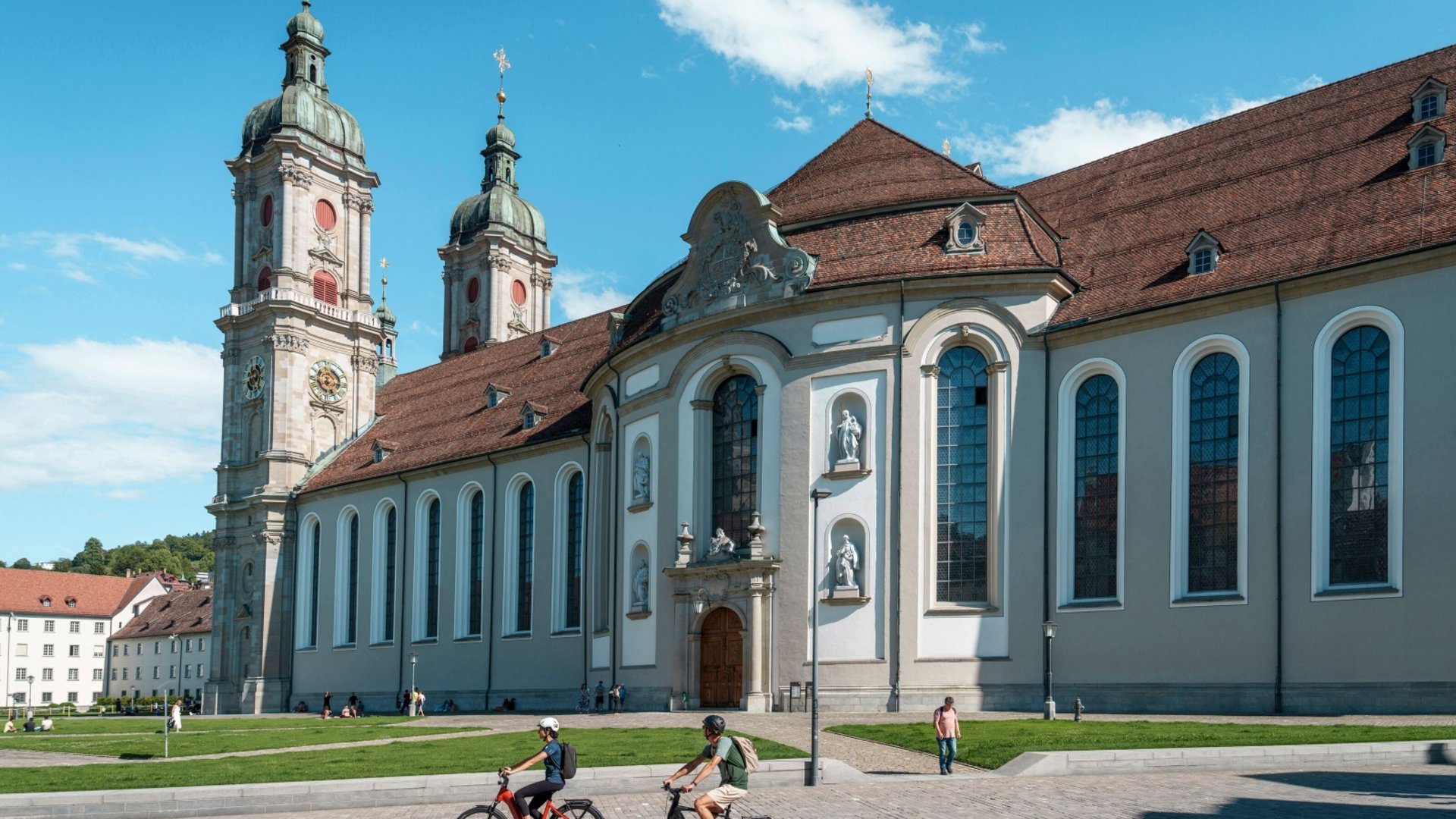 Two cyclists in front of a historic church with red roof and blue windows