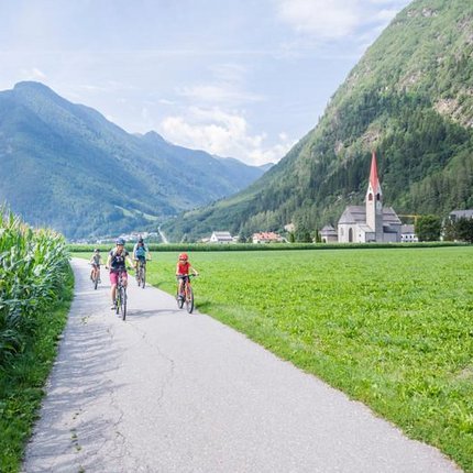 Family biking on rural path with mountains and church in background