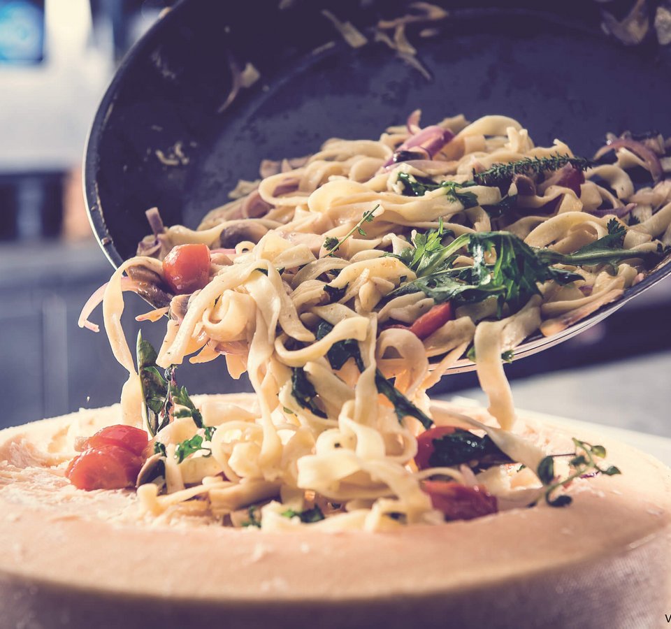 Pasta with vegetables being served inside a large cheese wheel