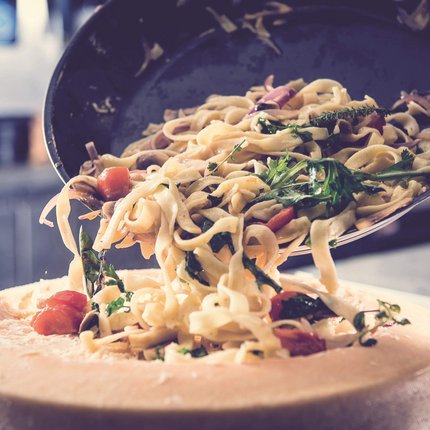 Pasta with vegetables being served inside a large cheese wheel