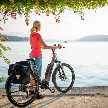 Frau mit Fahrrad blickt auf ruhigen See und Berge bei Sonnenuntergang