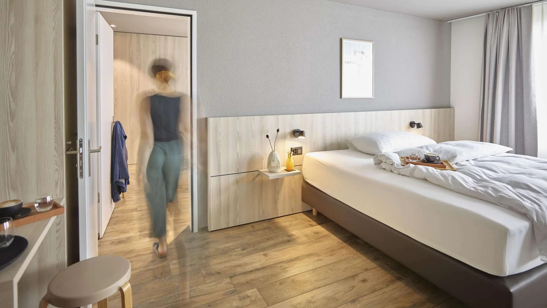 Modern bedroom with wooden floor and blurred person in doorway