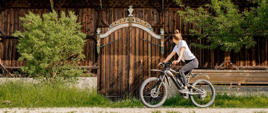 3 Gründe fürs Herbst-Radln in Inn-Salzach © Tourismusverein Inn-Salzach Frau auf Fahrrad blickt auf eine verzierten Holztür an einem Bauernhaus