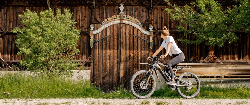 Frau auf Fahrrad blickt auf eine verzierten Holztür an einem Bauernhaus