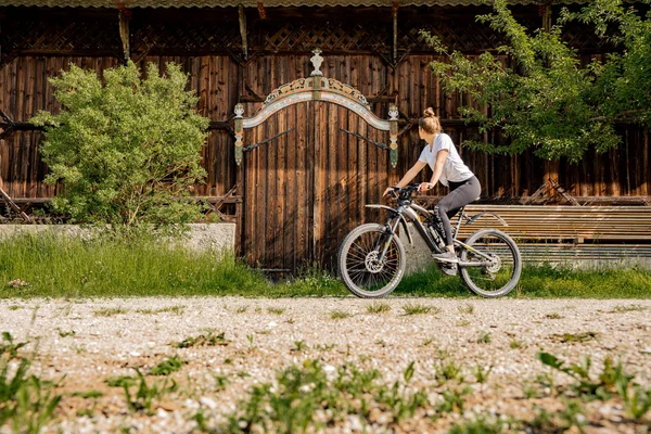 Frau auf Fahrrad blickt auf eine verzierten Holztür an einem Bauernhaus