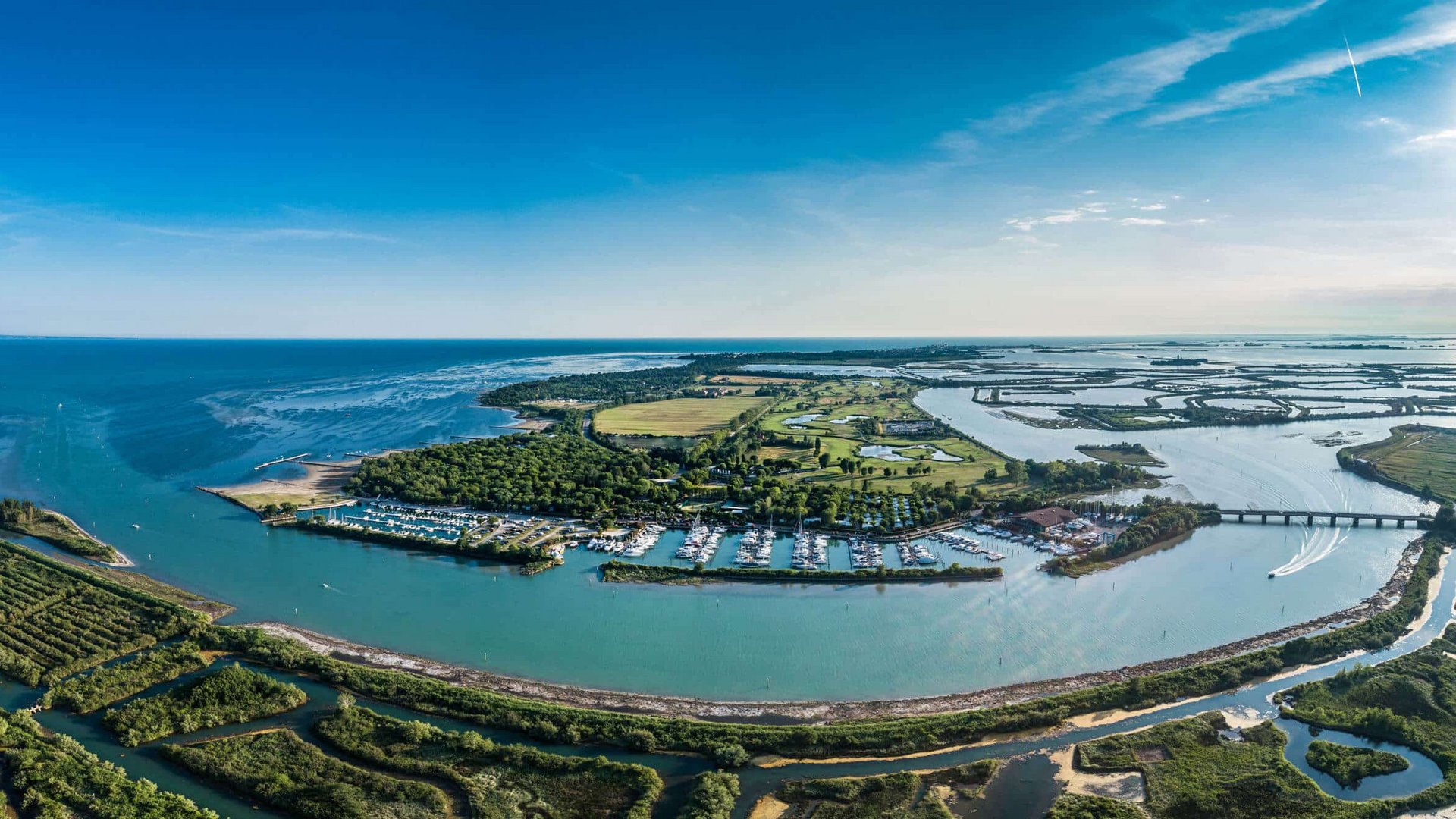 Aerial view of coastline with harbor, river mouth, and wooded areas under a sunny sky