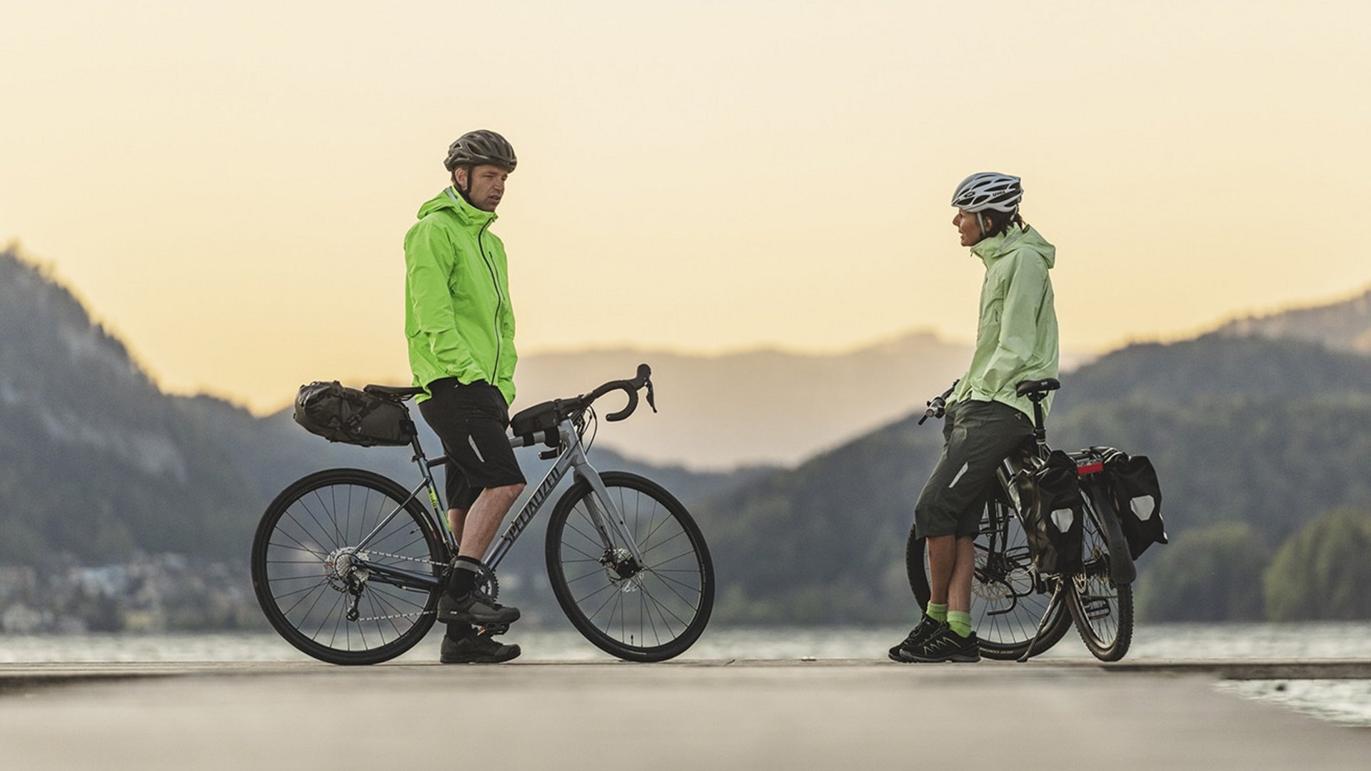 Schöffel © Zooom.at Two cyclists in green jackets standing with their bikes on a lakeside pier