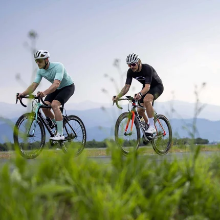 Three cyclists riding on a rural road with mountains in the background
