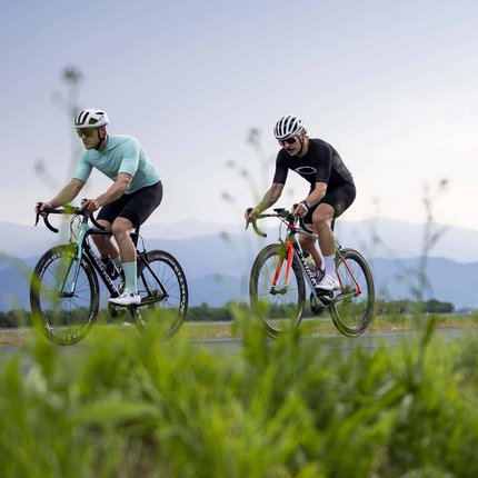 Three cyclists riding on a rural road with mountains in the background