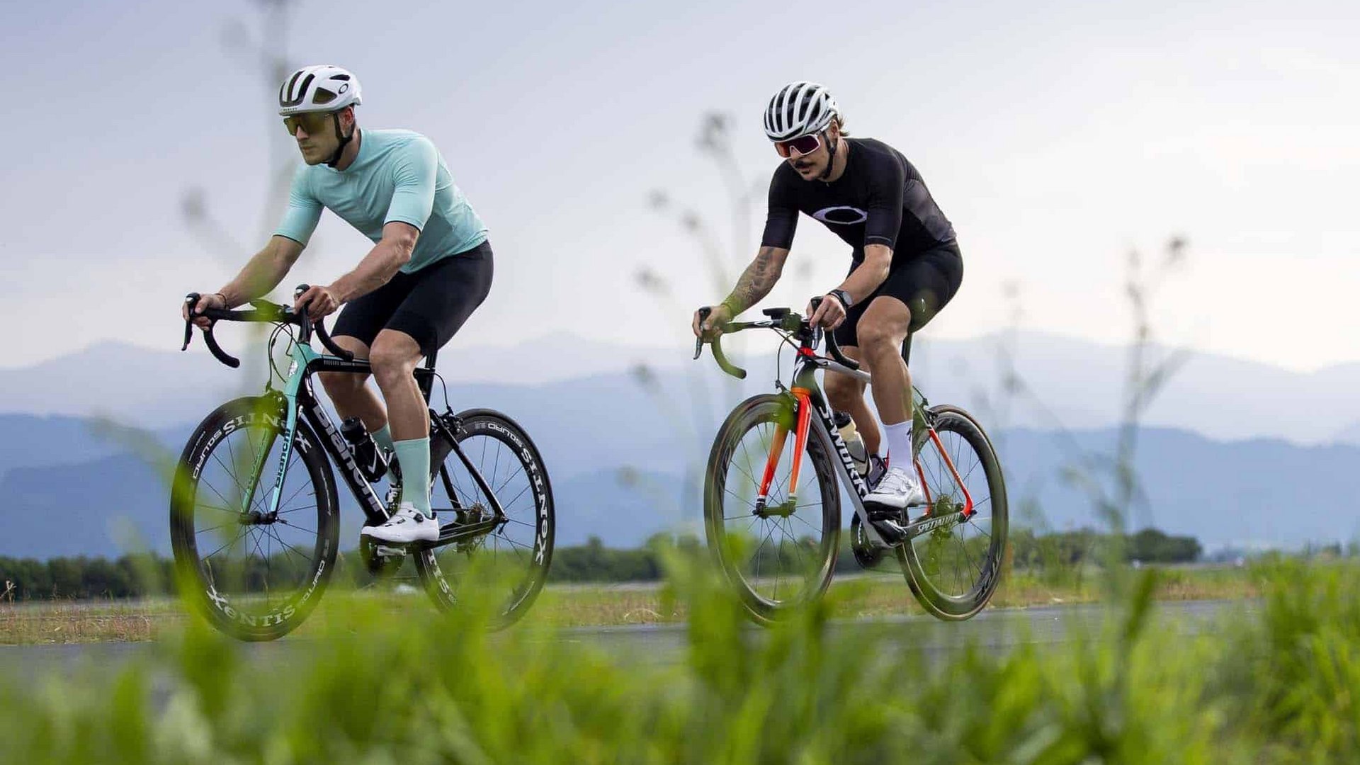 Three cyclists riding on a rural road with mountains in the background
